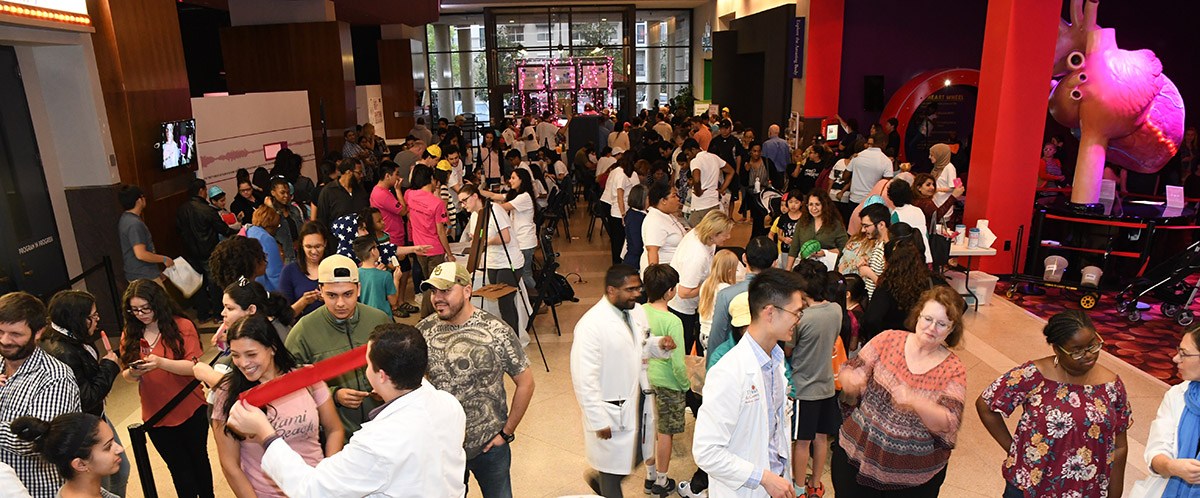 Many people milling about in a long entance way with multiple displays of brains and brain functions. Includes several medical personel in white smocks. 